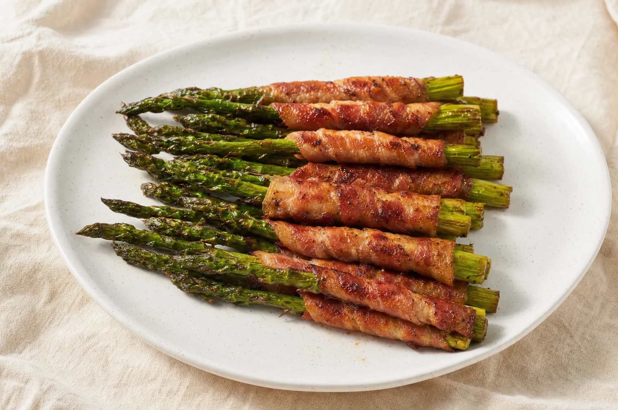 Bacon-wrapped asparagus spears on a white ceramic plate, bacon golden-brown and crispy