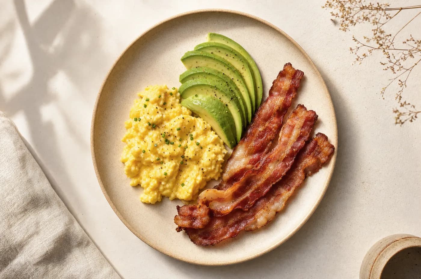 A plate of soft scrambled eggs, sliced avocado, and crispy bacon
