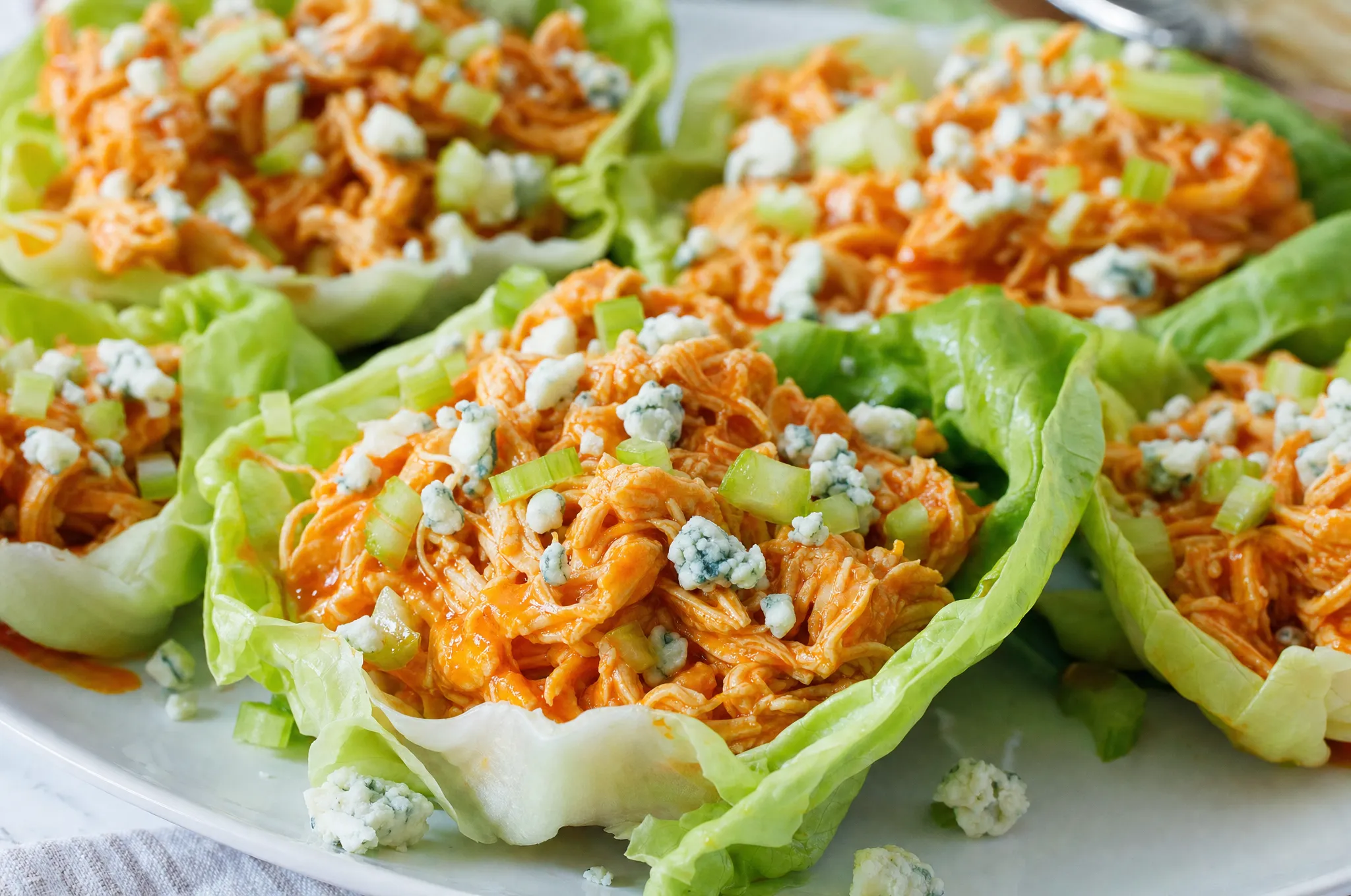 Keto slow cooker shredded buffalo chicken in glossy orange sauce served in crisp lettuce cups with blue cheese crumbles and celery