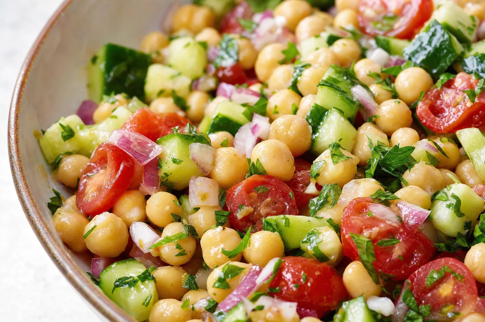 Mediterranean chickpea salad with cucumber, cherry tomatoes, red onion, and parsley tossed in a lemon-olive-oil dressing in a white bowl