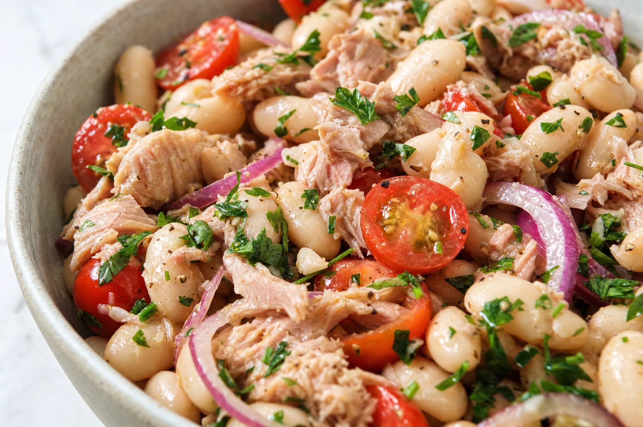 Mediterranean tuna and white bean salad with cannellini beans, cherry tomatoes, red onion, and parsley in a lemon-olive-oil dressing in a white bowl
