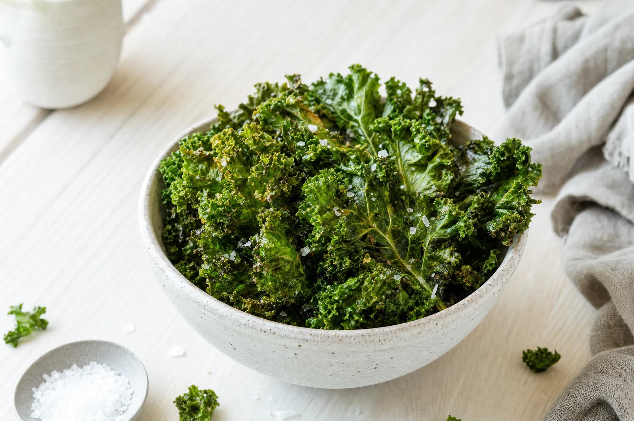 Crispy air fryer kale chips, lightly salted, in a pale stoneware bowl
