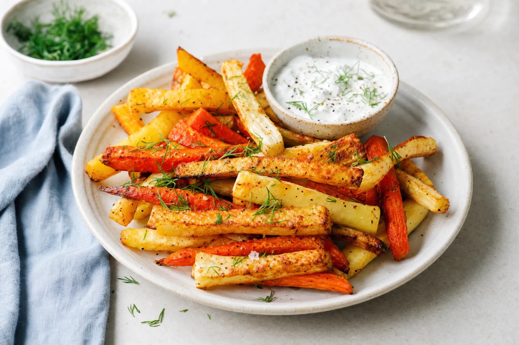Crispy air fryer root vegetable fries — carrot, parsnip, and rutabaga — with dill and a yogurt dip on a pale stoneware plate