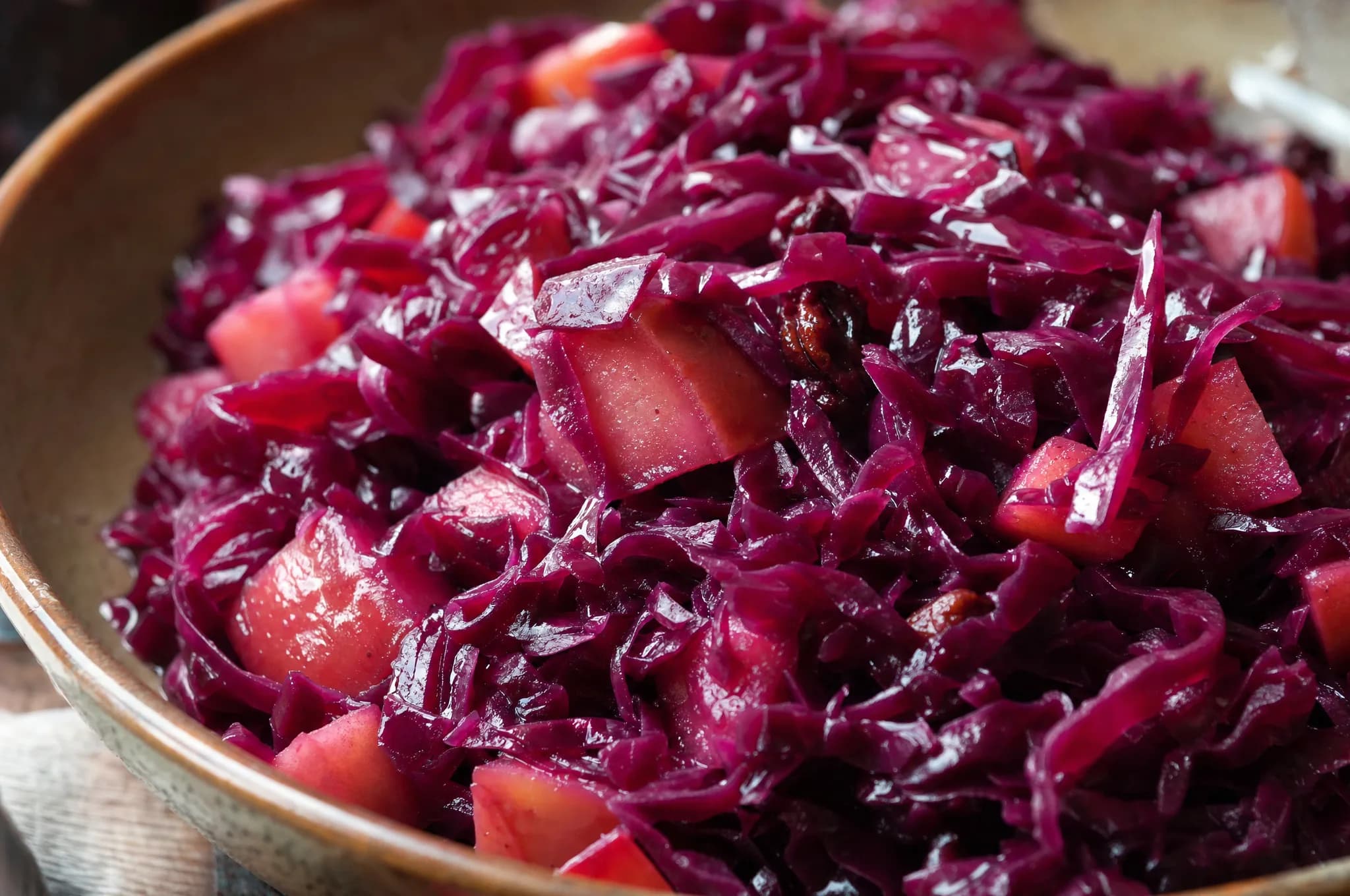 A bowl of deep-purple braised red cabbage flecked with apple, served beside sliced roast on a rustic table