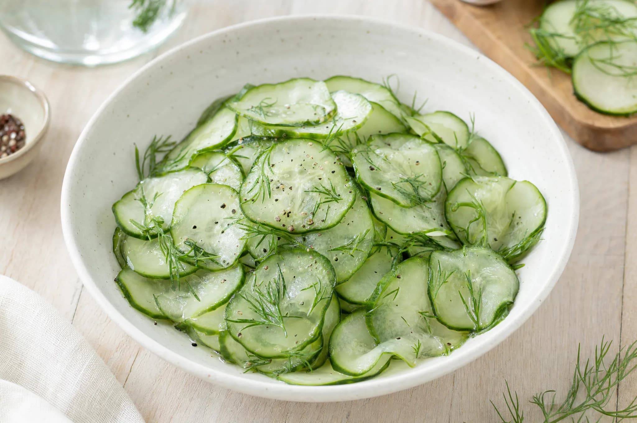 Swedish pickled cucumber salad with thinly sliced cucumbers in vinegar, fresh dill, and cracked pepper in a shallow pale bowl
