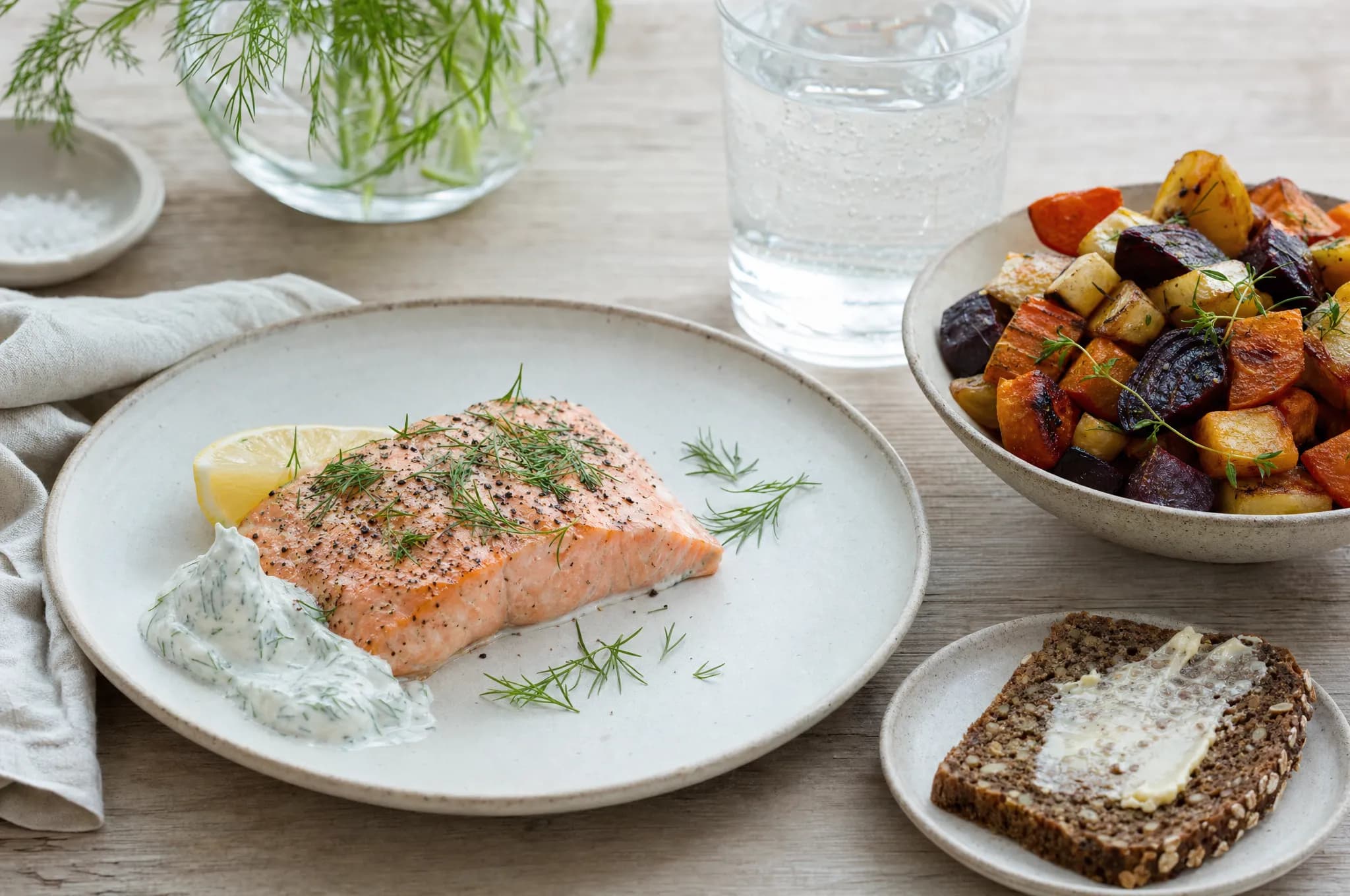 A Nordic dinner spread with baked salmon, roasted root vegetables, and rye bread on a light wood table