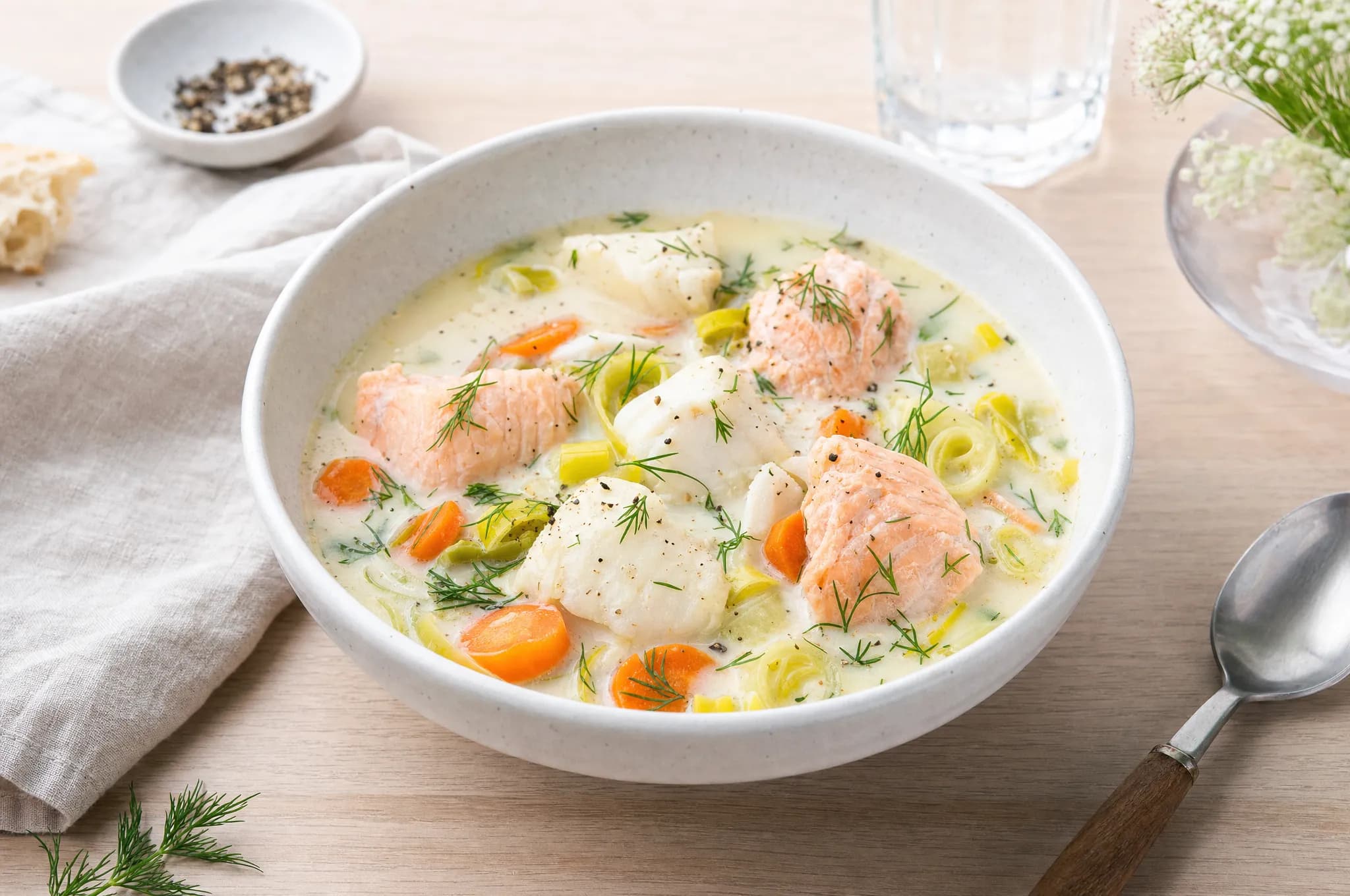 Creamy Norwegian fish soup with chunks of salmon and cod, carrots, leeks, and fresh dill in a pale stoneware bowl