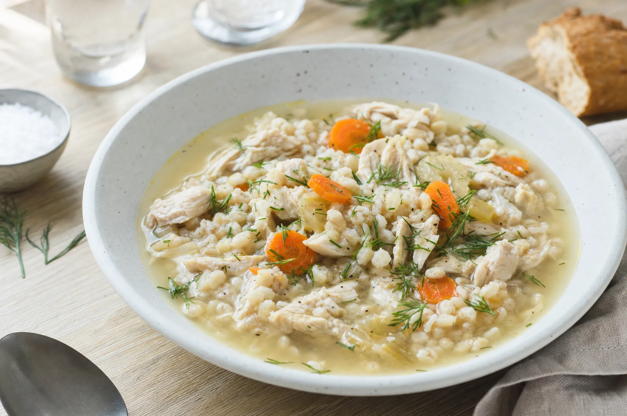 A pale stoneware bowl of hearty Nordic chicken and barley soup with carrots and fresh dill