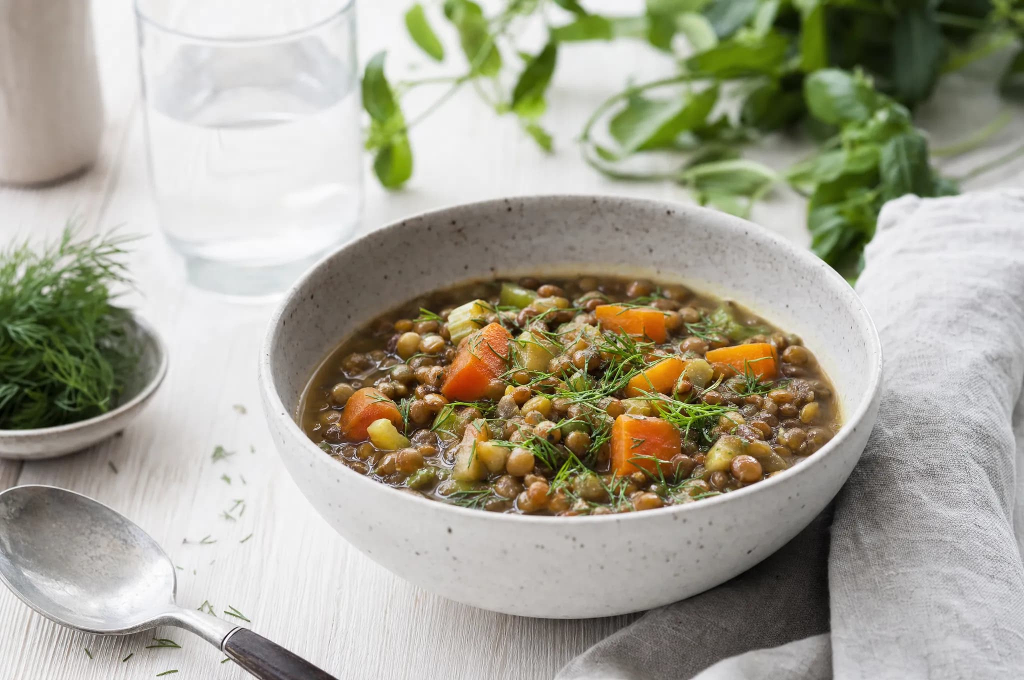 A pale stoneware bowl of hearty Nordic lentil stew with carrots, celery, and fresh dill