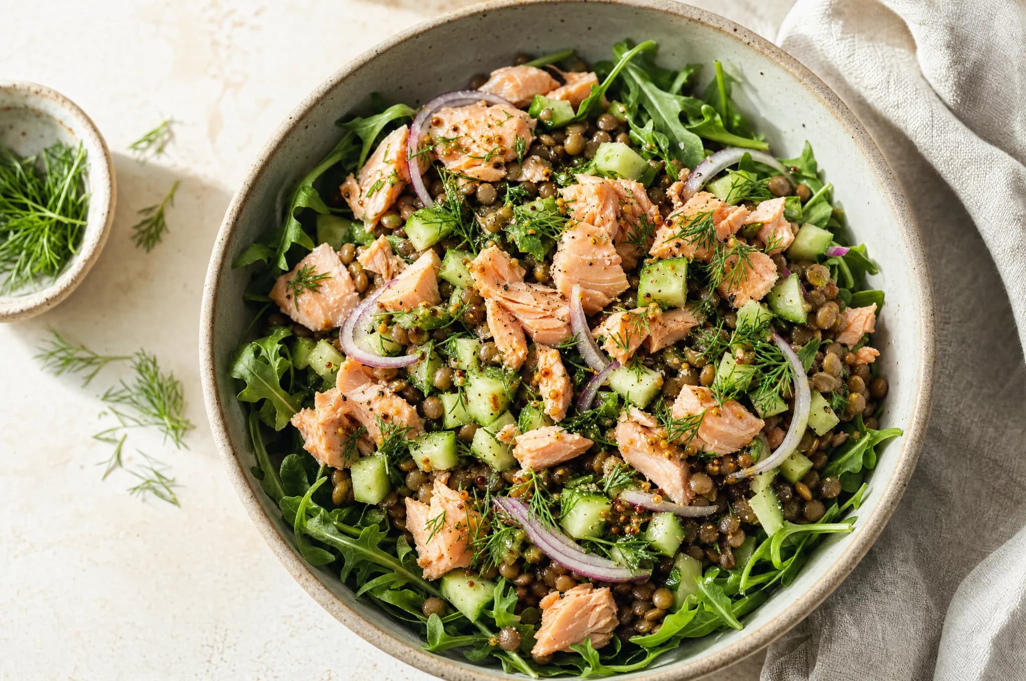 A bowl of lentil salad topped with flaked salmon, diced cucumber, red onion, and fresh dill, drizzled with a mustard vinaigrette