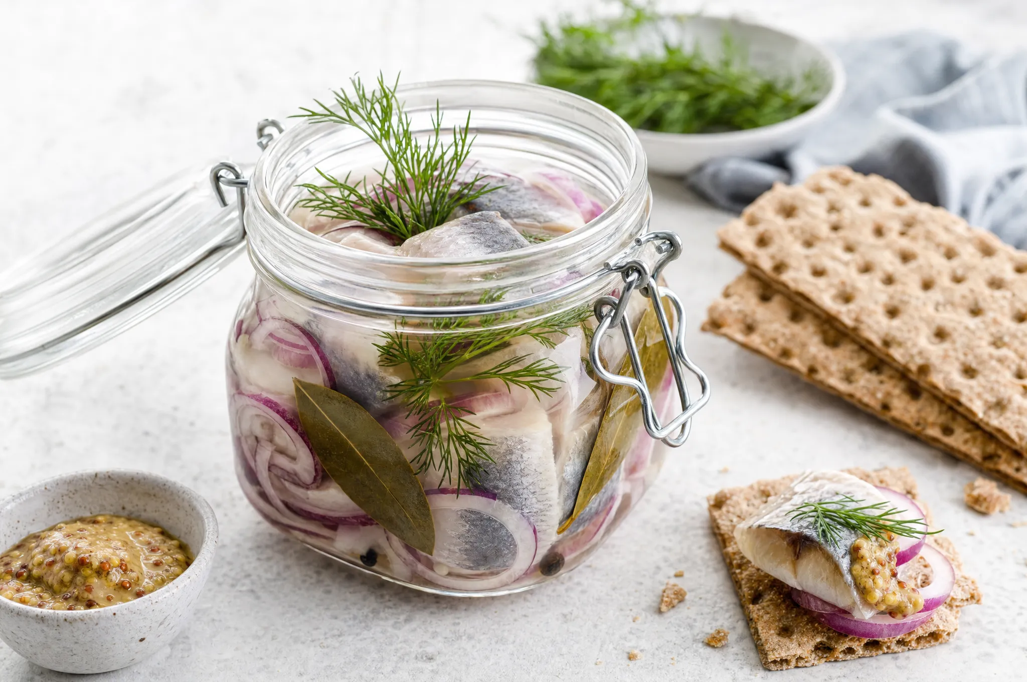 Nordic pickled herring in a glass jar with onion rings, dill, and bay leaves, served on crispbread with mustard