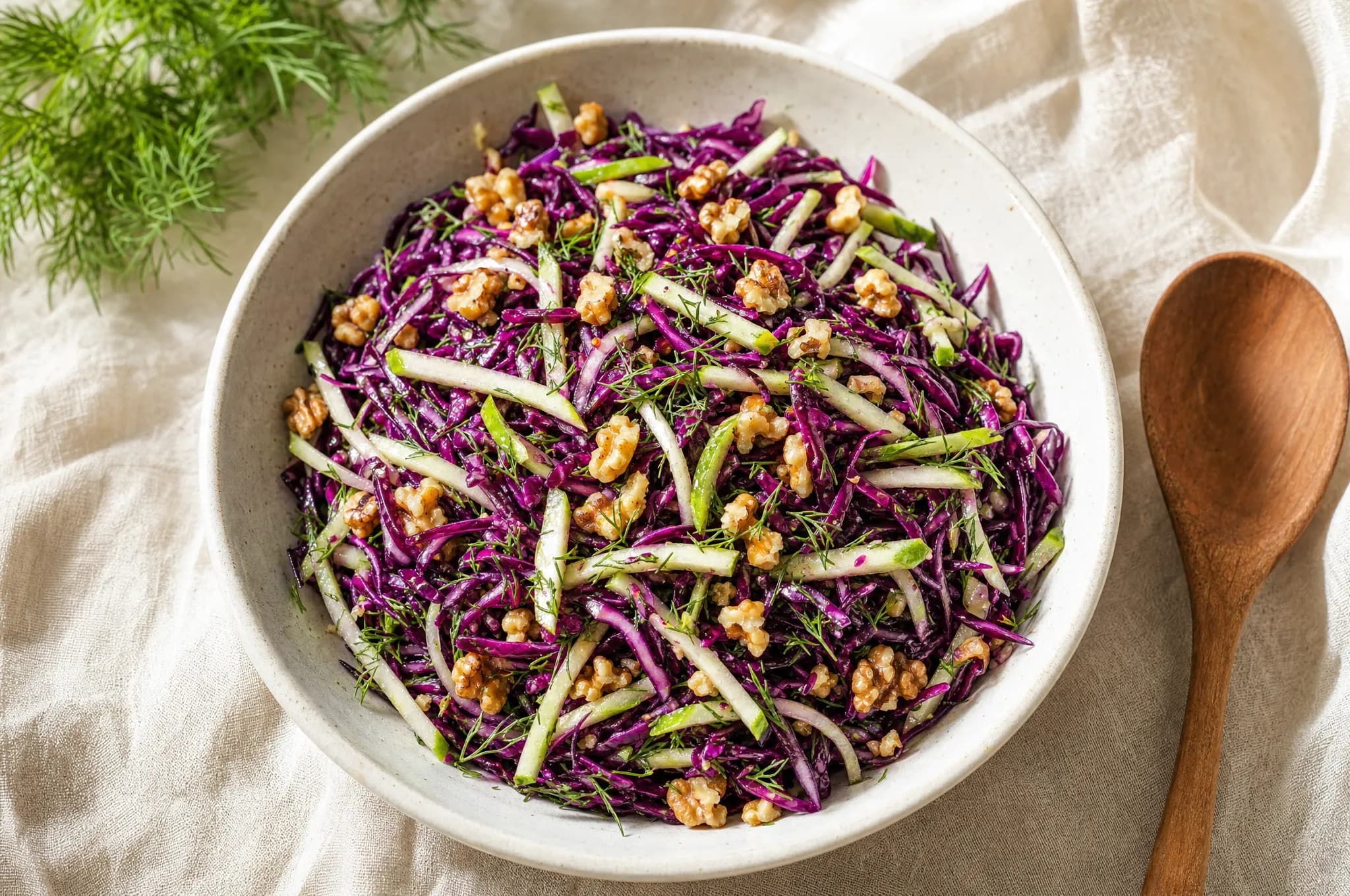 A bowl of shredded red cabbage and julienned green apple salad with chopped walnuts and fresh dill in a light dressing