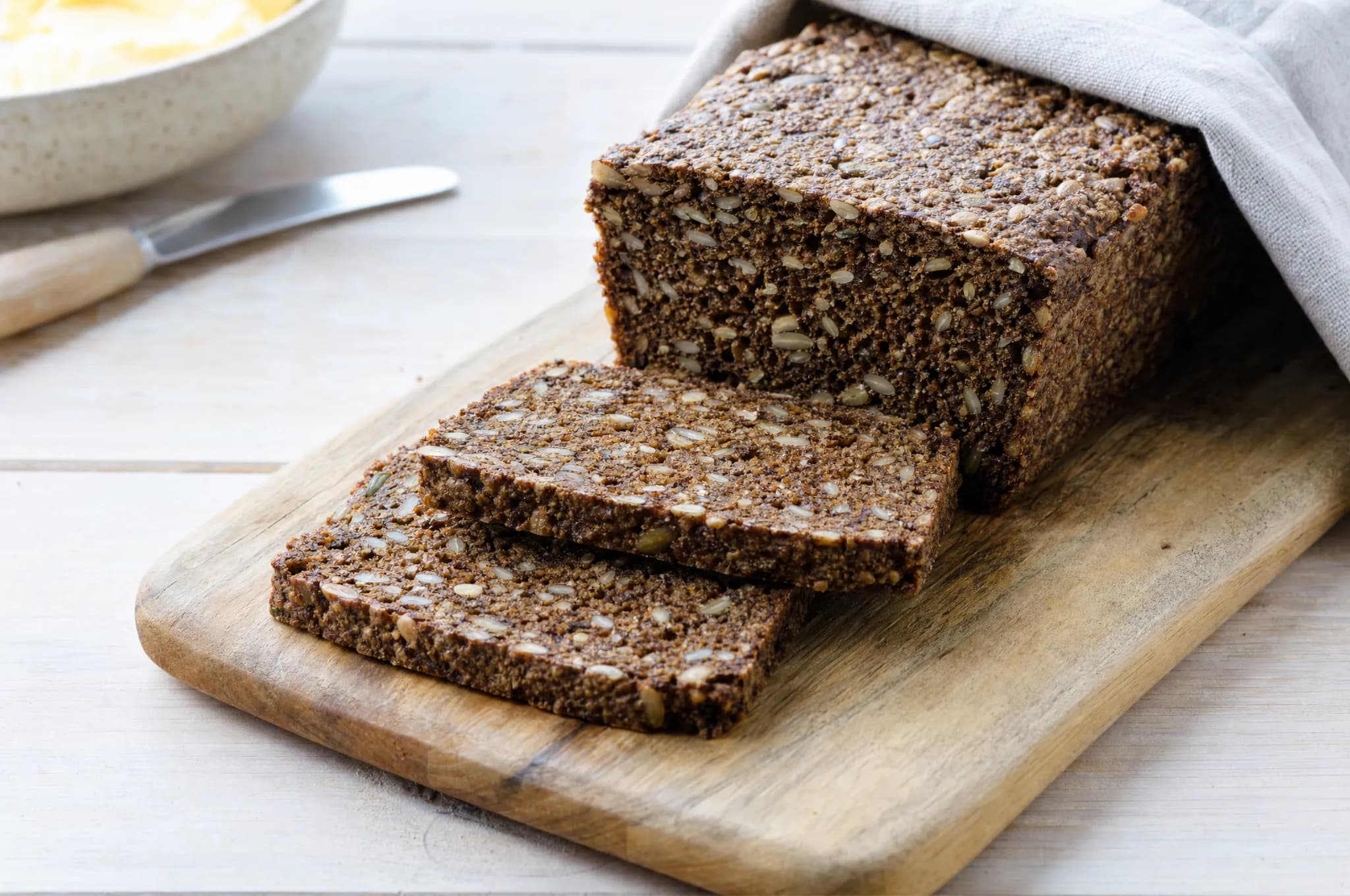 A sliced loaf of dense dark Danish rye bread packed with seeds on a wooden cutting board