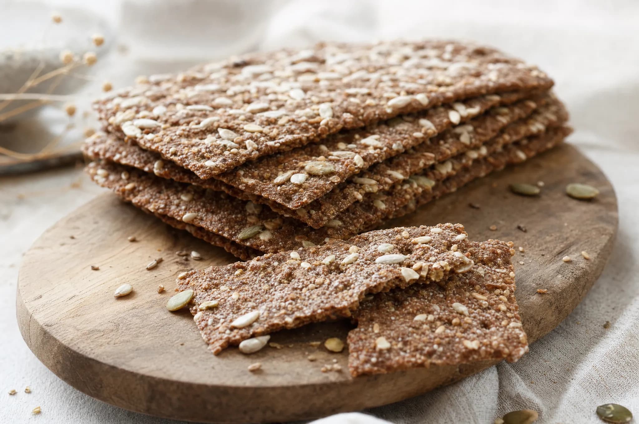 Stacked Nordic rye crispbread crackers with seeds on a wooden board, one broken to show the thin crisp texture