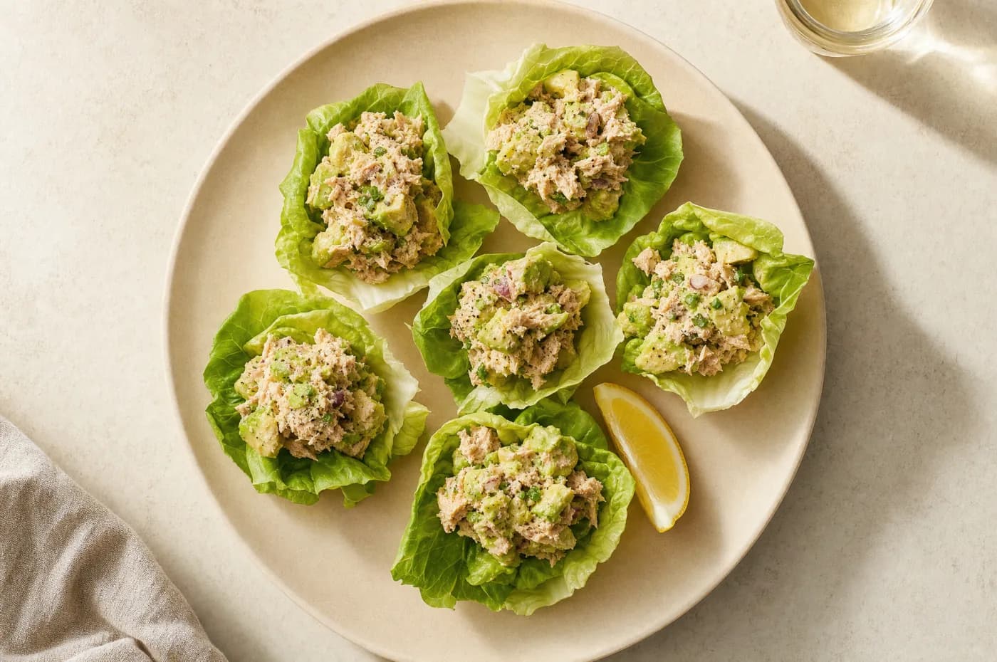 Six little-gem lettuce cups filled with avocado tuna salad, a lemon wedge alongside