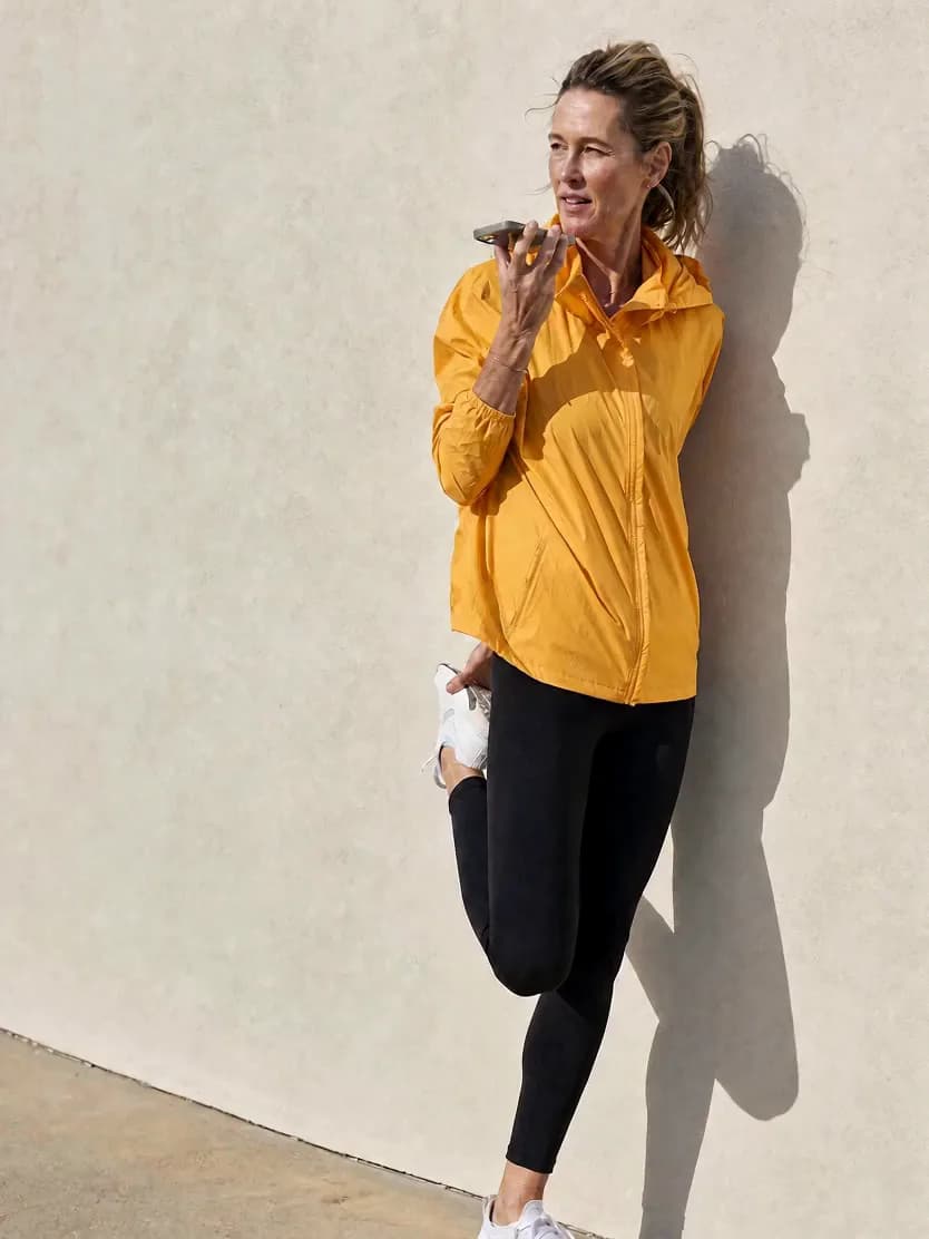 A woman recording a voice note after a run, in a mustard windbreaker
