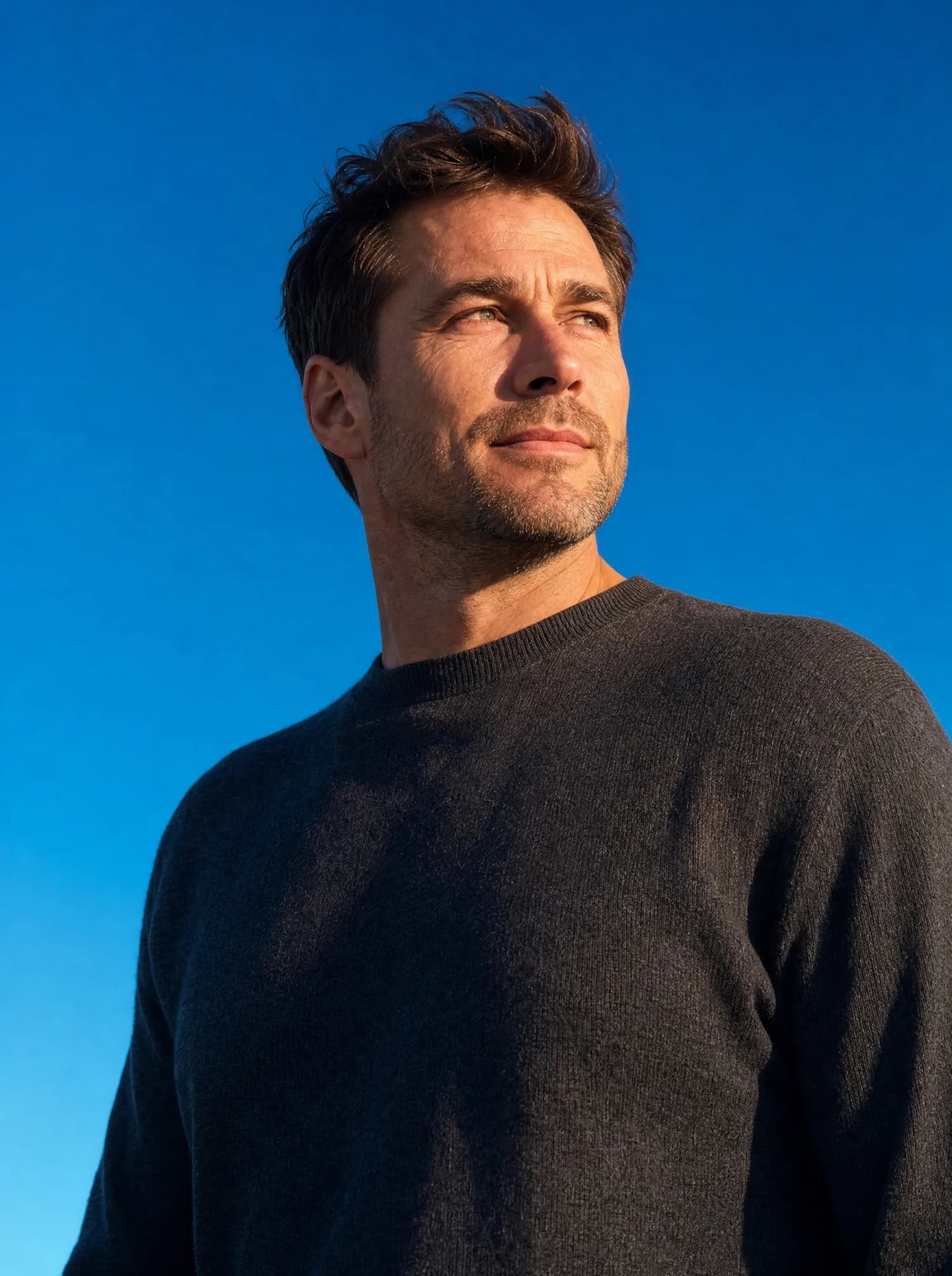 A man in a charcoal wool sweater against a clear blue sky